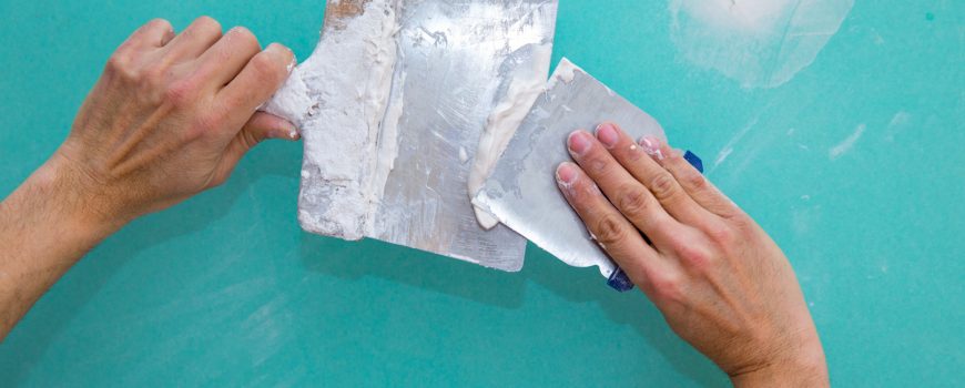 Plastering man hands with plaste on drywall plasterboard